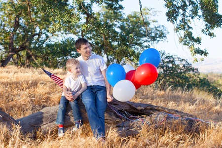 handsome father holding colorful balloons and his little son holding american flag celebrating 4th of Julyの写真素材
