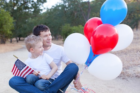 handsome father holding colorful balloons and his little son holding american flag celebrating 4th of Julyの写真素材