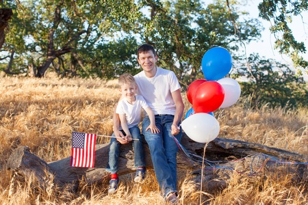 handsome father holding colorful balloons and his little son holding american flag celebrating 4th of Julyの写真素材