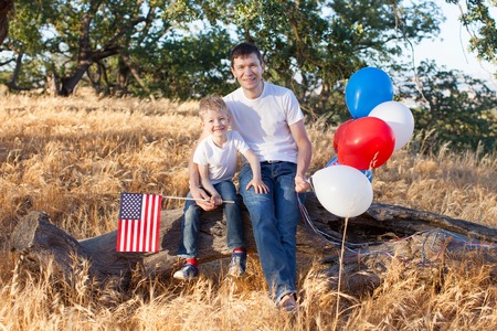 handsome father holding colorful balloons and his little son holding american flag celebrating 4th of Julyの写真素材