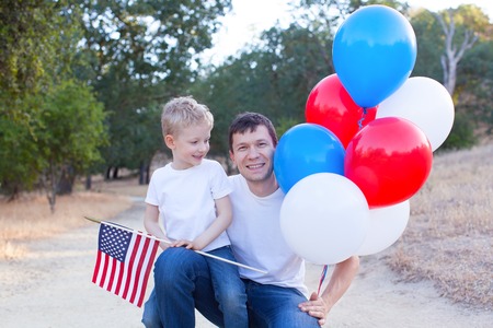 handsome father holding colorful balloons and his little son holding american flag celebrating 4th of Julyの写真素材