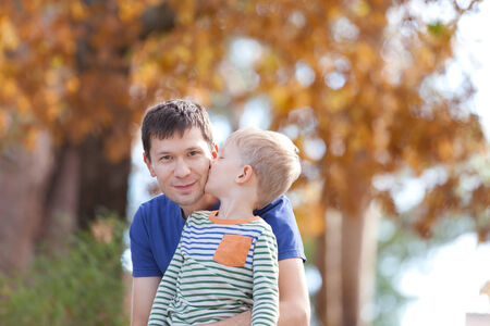 little son kissing his father at the park at fall timeの写真素材