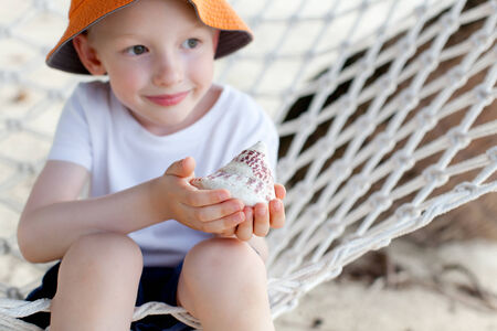 curious little boy holding shell at the beachの写真素材