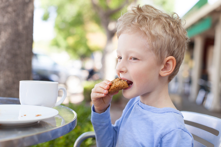 happy cheerful boy enjoying cookie in outdoor cafeの写真素材