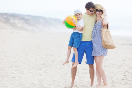 family of three enjoying fun day at the beach together playing with the beach ballの写真素材