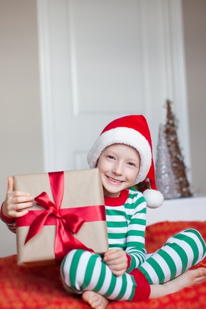 excited little boy in santa hat at christmas time at home holding nicely wrapped presentの写真素材