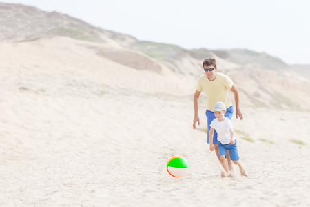 cheerful family of two playing with ball at the beachの写真素材