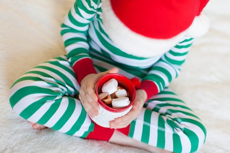 cute smiling boy sitting cozy at home, holding cup of hot cocoa at christmas timeの写真素材