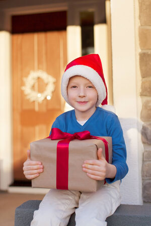 smiling cheerful boy with christmas present by the decorated houseの写真素材