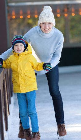 young mother and her son ice skating together at outdoor skating rink at winterの写真素材