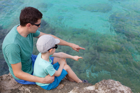 young father and his son sitting at the rocky beach and exploring underwater lifeの写真素材