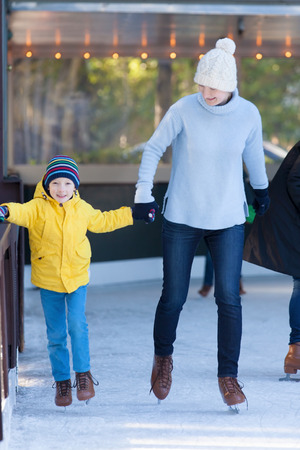 young mother and her son ice skating together at outdoor skating rink at winterの写真素材