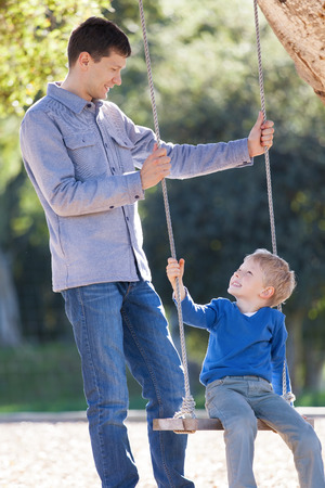 loving family of two having fun swinging in the parkの写真素材