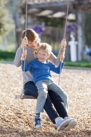 loving family of two having fun swinging in the parkの写真素材
