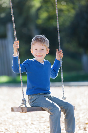 smiling positive little boy swinging in the park at summerの写真素材