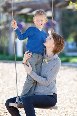 beautiful young mother and her little son enjoying time together and having fun in the park swingingの写真素材