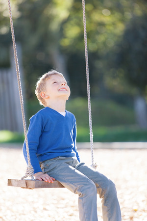 smiling little boy sitting at the swings and dreamingの写真素材