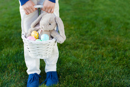 child holding basket with colorful easter eggs and bunny toy at spring time in the parkの写真素材