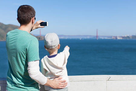family of two enjoying the view of famous san francisco sightseeing - golden gate bridge and taking picture with phoneの写真素材