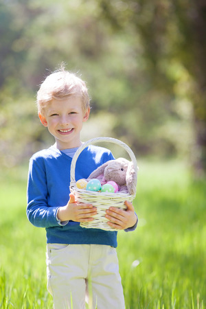 little smiling boy holding basket with easter eggs and bunny after egg hunt in the parkの写真素材