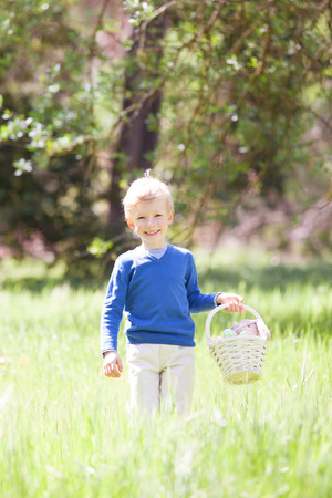 little smiling boy holding basket with easter eggs and bunny after egg hunt in the parkの写真素材