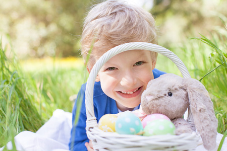 little smiling boy holding basket with easter eggs and bunny after egg hunt in the park lying in the...