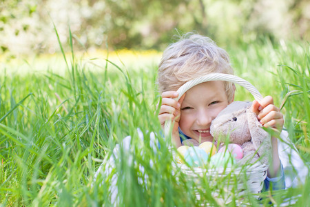 little smiling boy holding basket with easter eggs and bunny after egg hunt in the park lying in the grassの写真素材