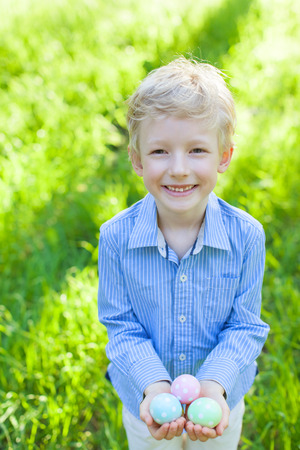 smiling little boy holding easter eggs after egg hunt at spring timeの写真素材