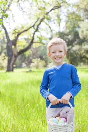 smiling little boy holding basket with easter eggs and bunny after egg hunt at spring timeの写真素材