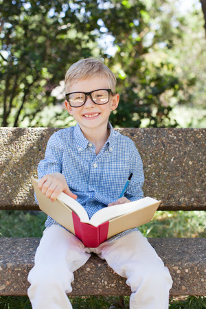 smiling little schoolboy in glasses holding book ready to go to school, back to school conceptの写真素材