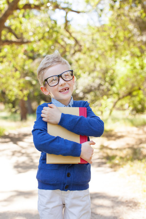 cute funny schoolboy in glasses holding book ready to go to school, back to school conceptの写真素材