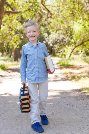smiling little schoolboy holding book and lunchbag ready to go to school, back to school conceptの写真素材