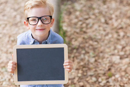 little smiling boy in cute glasses holding empty chalkboard, back to school concept