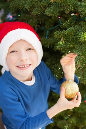 excited little boy in santa's hat helping with christmas tree decorations at christmas timeの写真素材