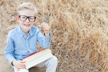 smart excited little boy in glasses studying with book and pencil ready for school, back to school...