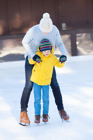 young mother teaching her positive son ice skating, enjoying winter time at outdoor skating rink togetherの写真素材