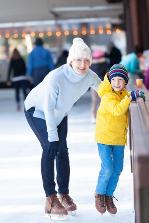 young mother teaching her positive son ice skating, enjoying winter time at outdoor skating rink togetherの写真素材