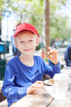 positive smiling boy enjoying desserts and hot cocoa in outdoor cafe, city lifestyleの写真素材