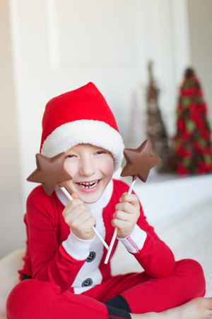 positive little boy in santa's hat and elf's costume holding star shaped candies ready for festive christmas timeの写真素材