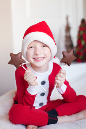 cheerful little boy in elf costume holding star shaped chocolate candies and enjoying cozy christmas time at homeの写真素材