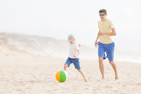 cheerful smiling son and his young father playing beach ball at the beach in californiaの写真素材