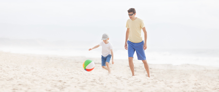cheerful smiling son and his young father playing beach ball at the beach in californiaの写真素材
