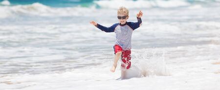 panorama of playful running boy playing in the waves at the beach at kauai, hawaiiの写真素材