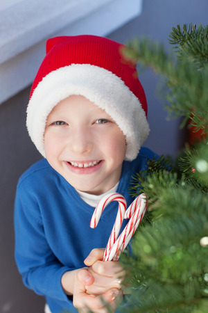 little smiling boy in santa's hat holding candy canes at christmas timeの写真素材