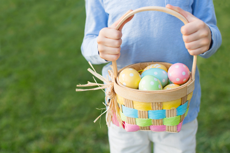 boy holding basket full of colorful easter eggs after egg hunt at spring timeの写真素材