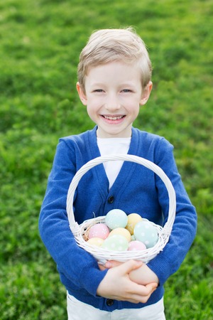 beautiful smiling boy holding basket with colorful eggs after easter egg hunt