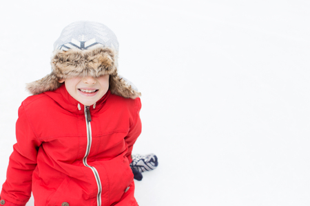 positive happy boy being silly and sitting on ice enjoying winter vacation at outdoor ice skating rinkの写真素材