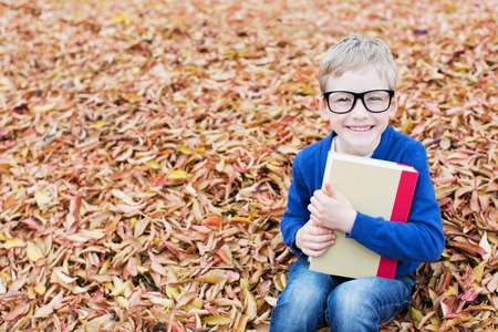 beautiful little schoolboy in glasses holding book ready for new school year in the autumn parkの写真素材