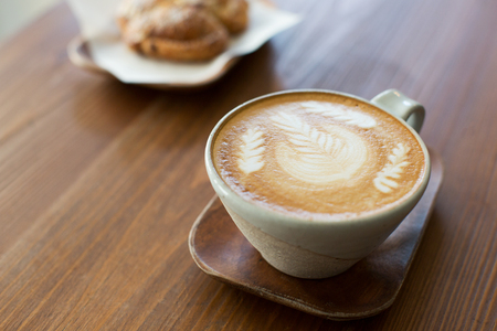 cup of latte coffee drink decorated with latte art and pastry at cafeの写真素材