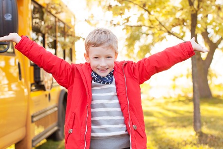 excited schoolboy standing by the school bus ready for new school yearの写真素材